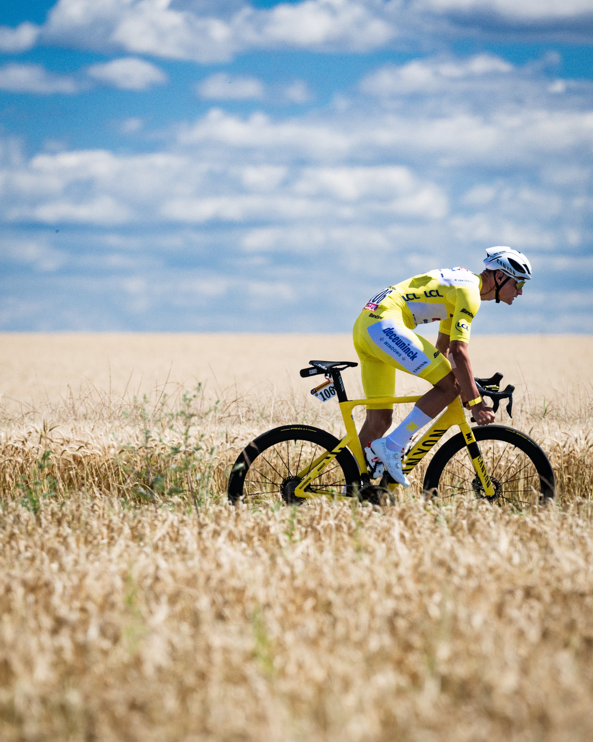 Cyclist in yellow Alpecin-Deceuninck kit riding through field